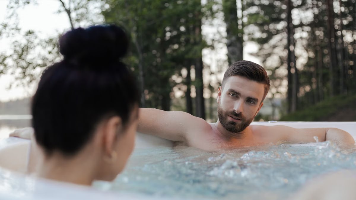 A couple enjoys a relaxing moment in an outdoor jacuzzi surrounded by trees, capturing a serene vacation vibe.